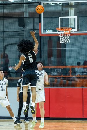 Player #5 in black uniform leaps to shoot basketball near the hoop during an indoor high school basketball game.