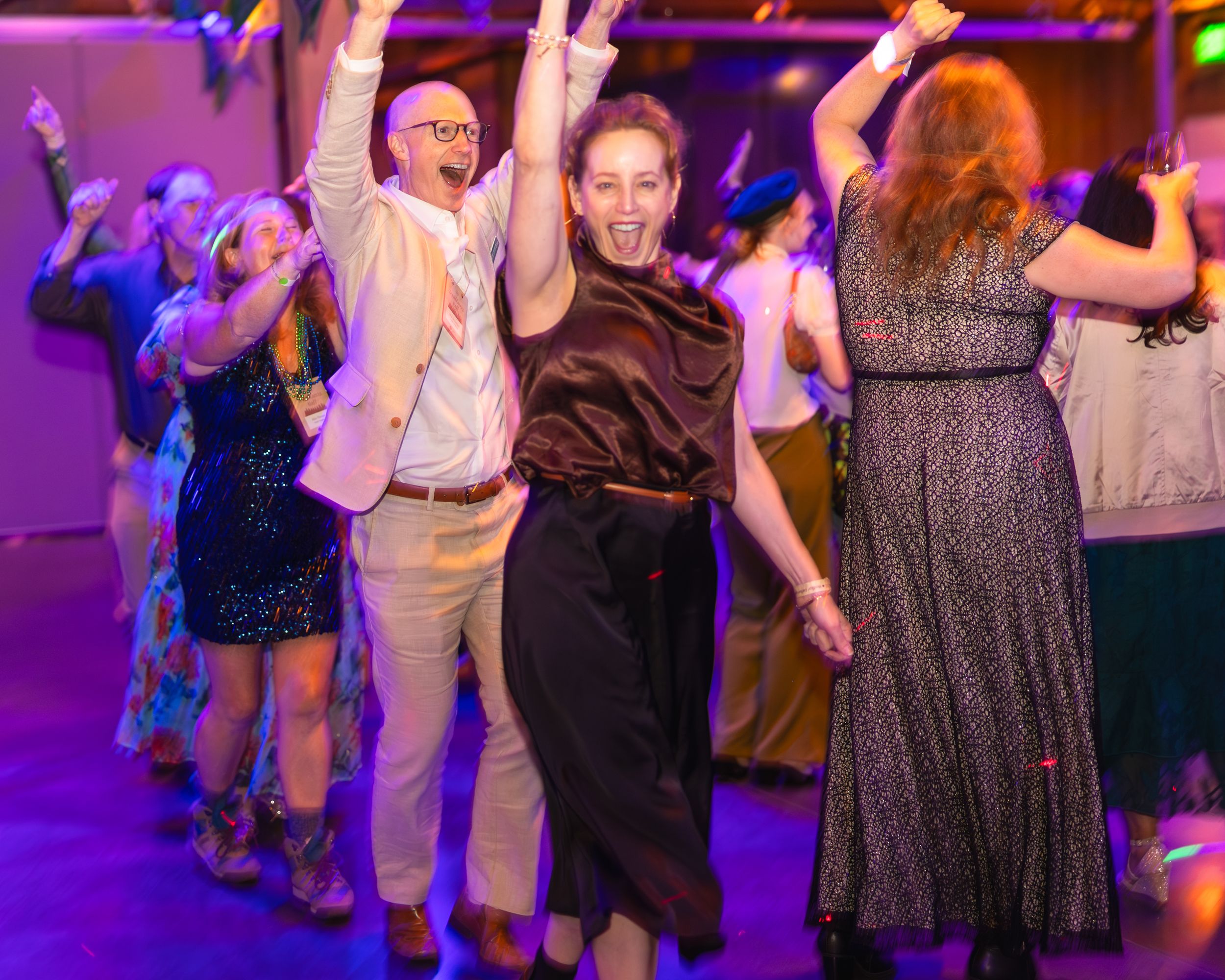 Guests dancing joyfully at an evening party, raising hands in celebration under colorful lights.