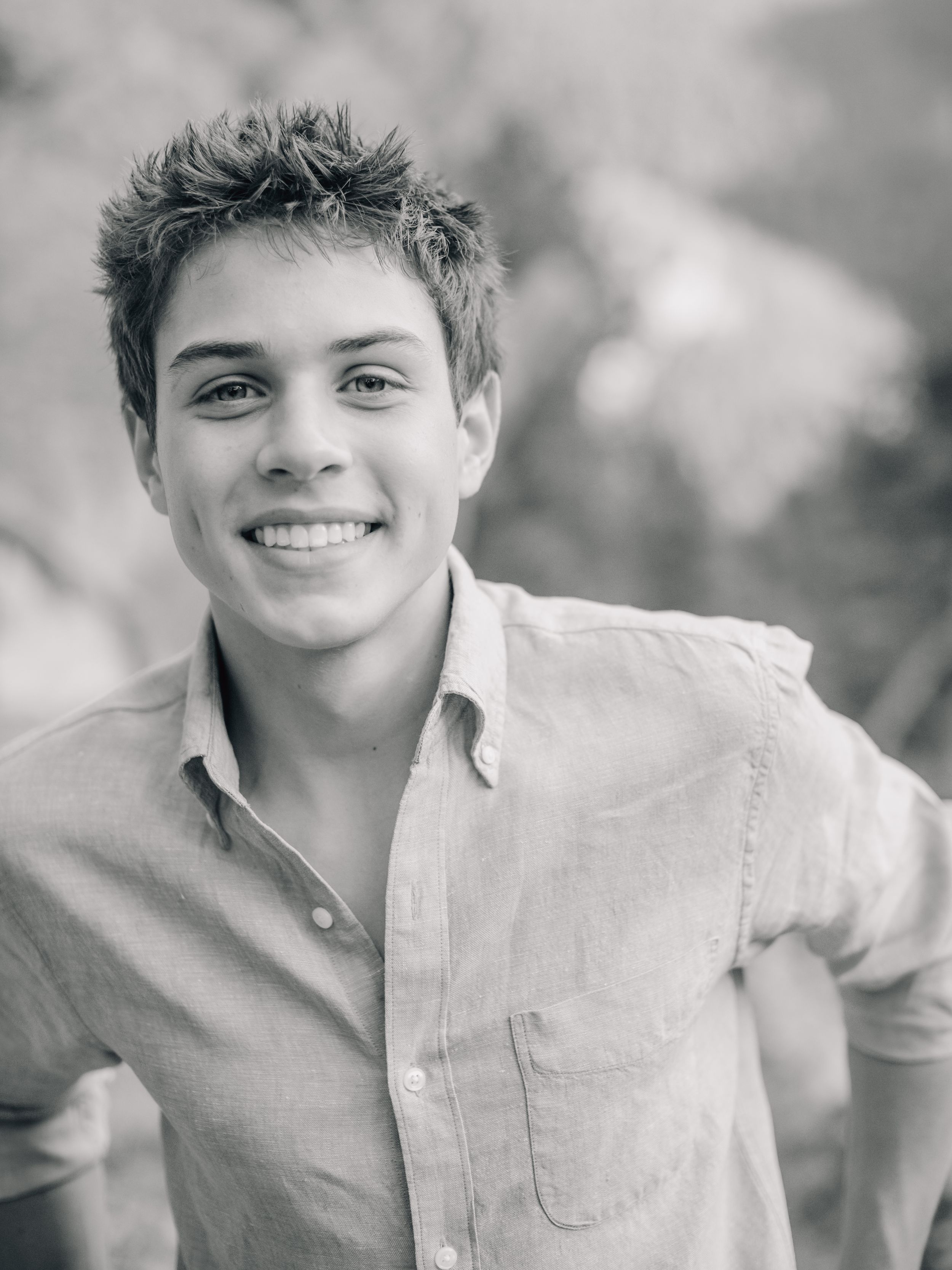 Black and white portrait of a young person in a casual button-down shirt with a bright smile outdoors.