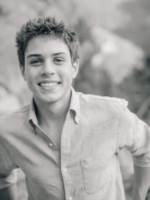 Black and white portrait of a young person in a casual button-down shirt with a bright smile outdoors.