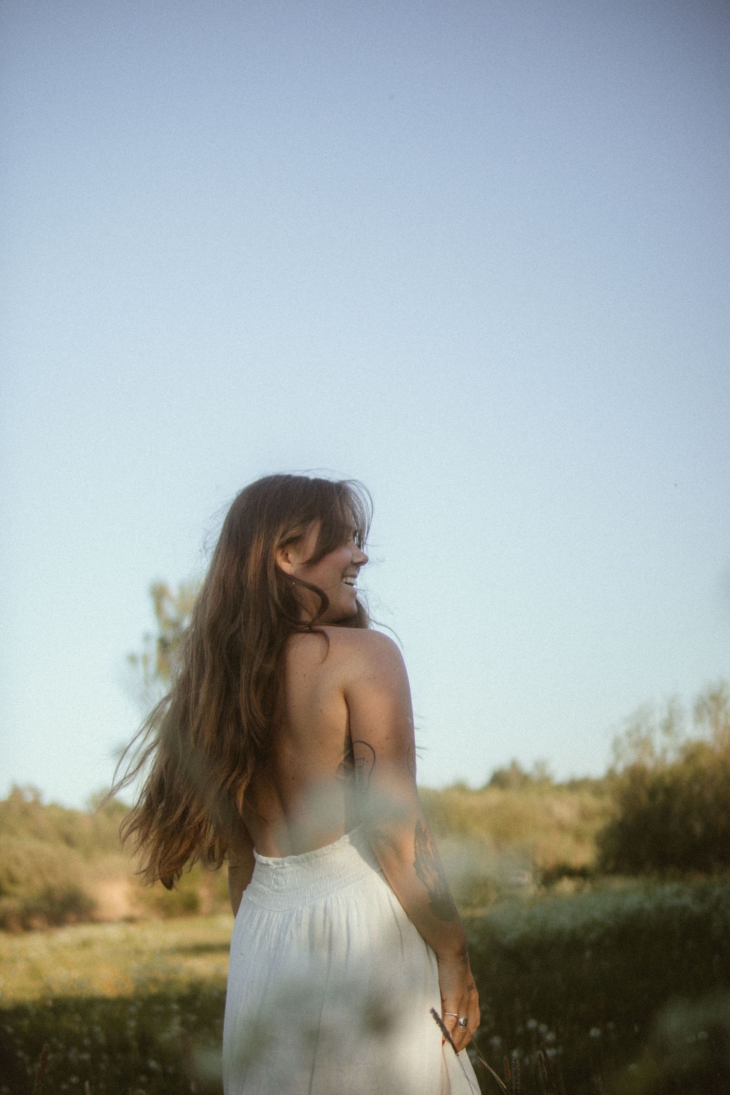 Dreamy backlit silhouette in white dress standing in golden summer field.