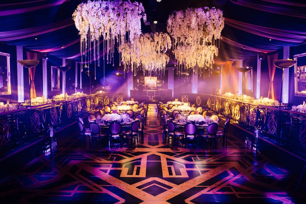 Luxurious wedding reception venue with hanging floral chandeliers and purple lighting.