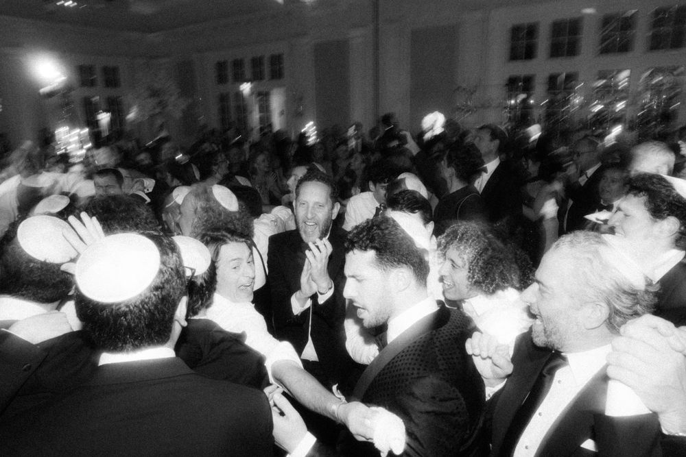 A blurred black and white photo of a crowded formal event with people dancing and celebrating.