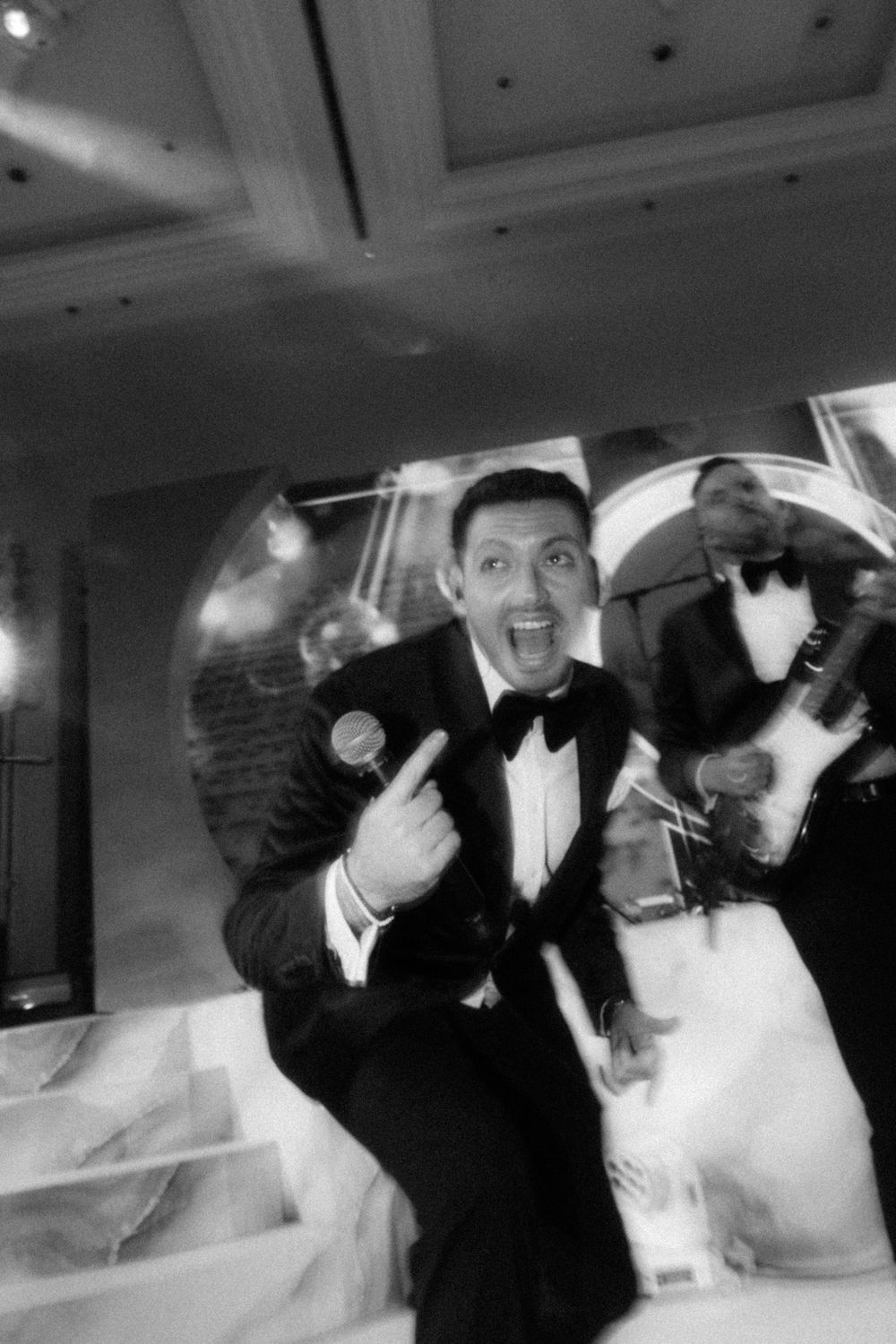 An energetic performer in a tuxedo gesturing excitedly during a formal event.