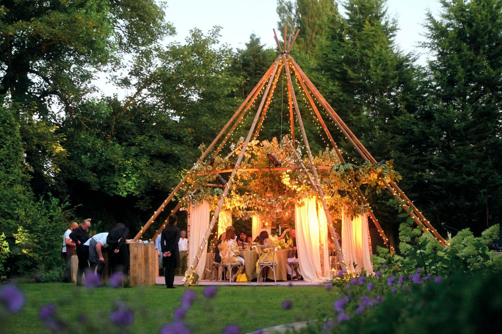 String lights illuminate an outdoor wedding tent creating a warm, romantic ambiance at dusk during a garden reception.