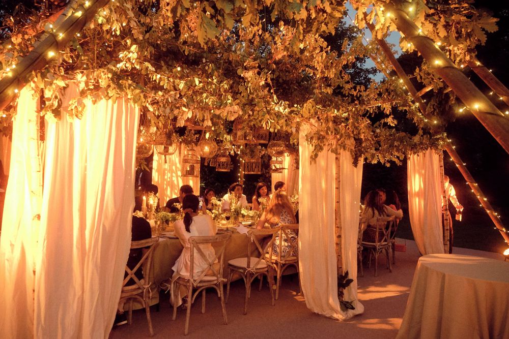 Romantic outdoor wedding reception with white drapes, twinkling lights, and floral decorations creating a dreamy atmosphere.