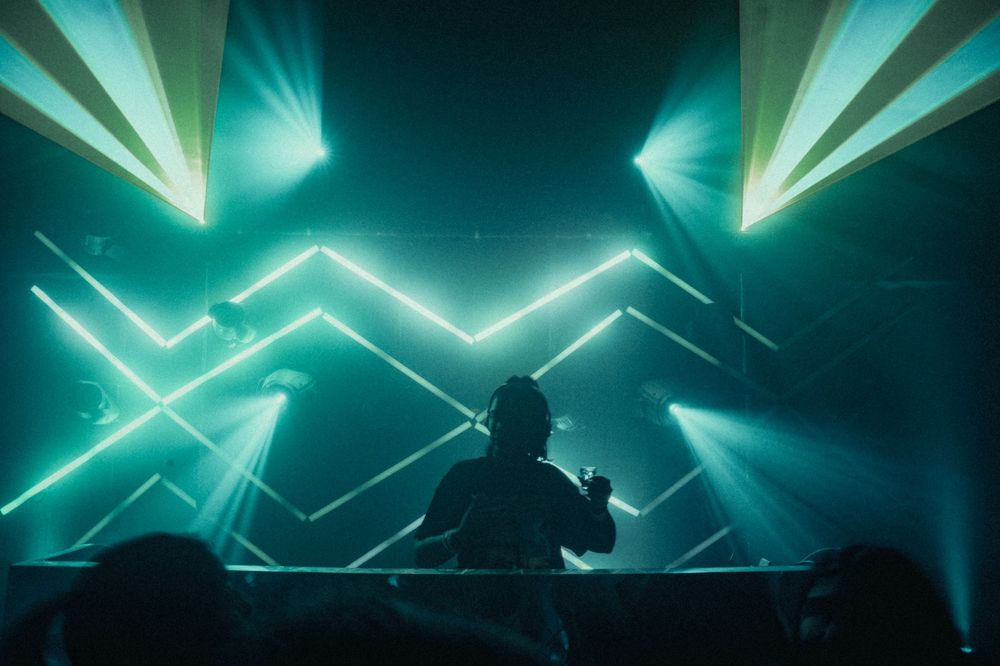 Dramatic stage lighting creates geometric patterns at an electronic music performance.