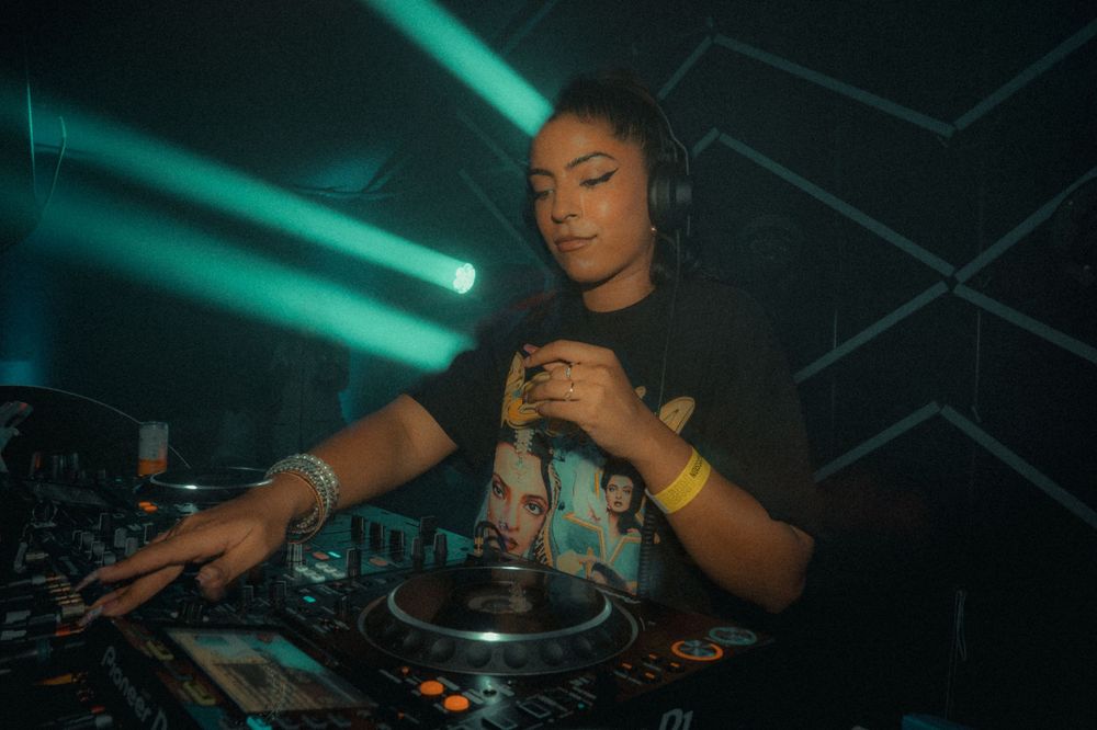 DJ performing at a turntable with green lighting effects in the background.