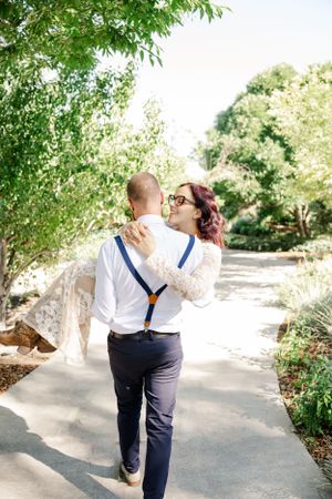 Couple embracing on garden path surrounded by green trees.