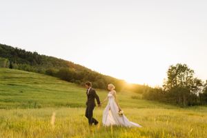 Romantic sunset wedding photo of couple walking through golden mountain meadow.