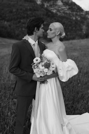 Elegant black and white wedding portrait with sunflower bouquet against mountain backdrop.