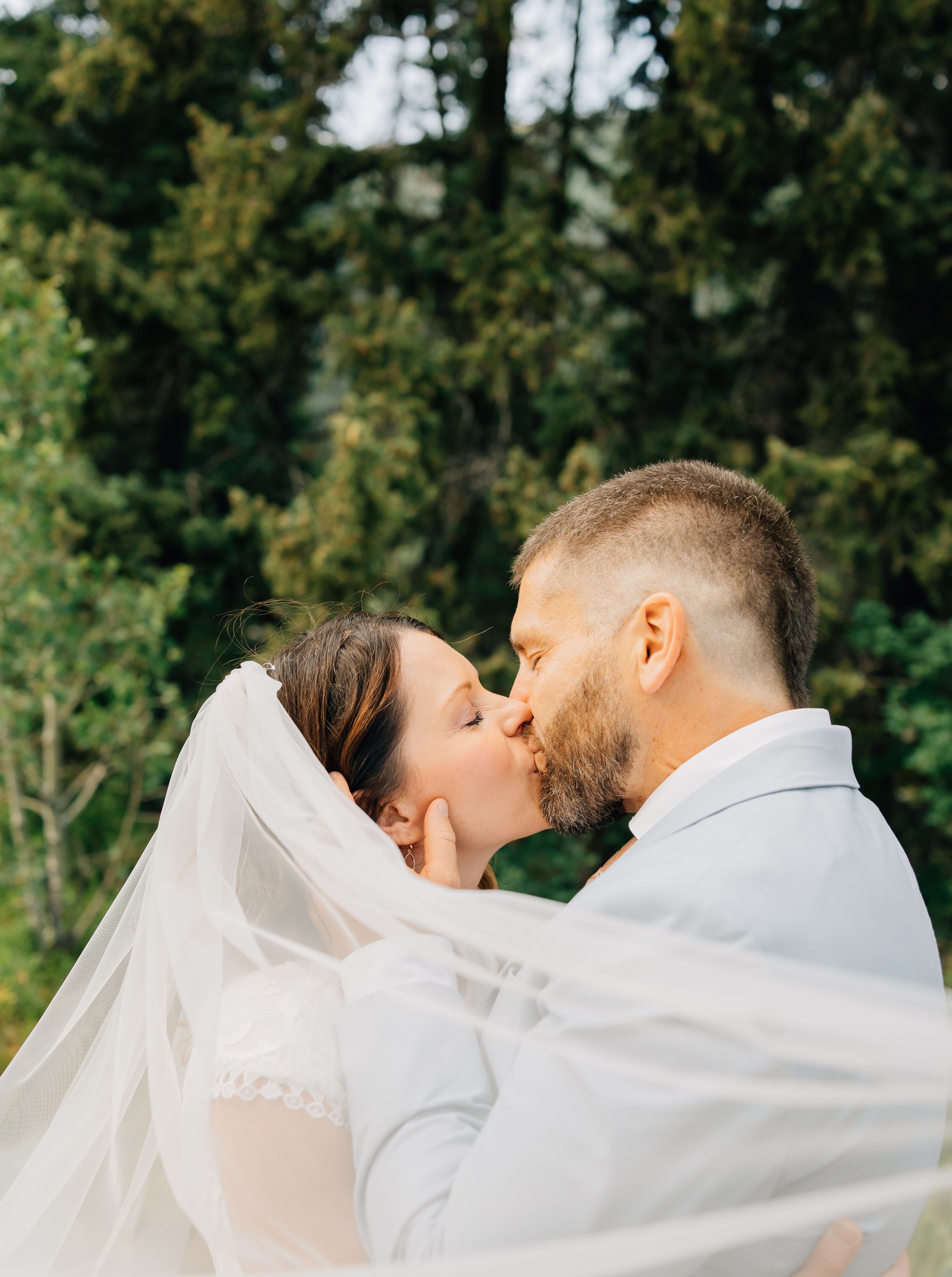 Intimate wedding moment captured as couple shares kiss under flowing veil.