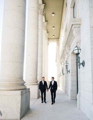 Two people in formal attire walking through classical colonnade.