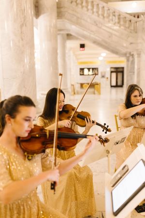 Musicians in gold dresses performing with violins in elegant hallway.