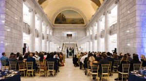 Elegant wedding ceremony venue with white columns and arched ceiling filled with seated guests.