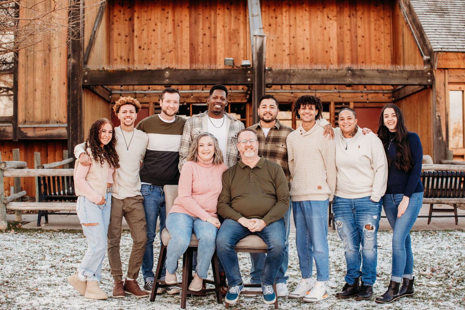 A large group portrait of people dressed in casual attire standing together outside a rustic building.