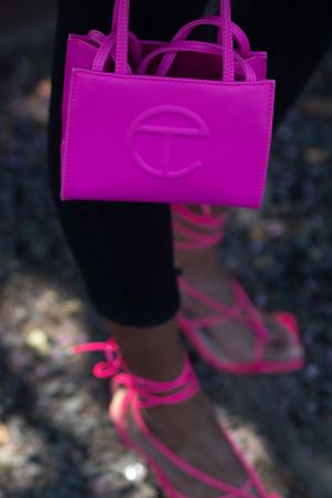 Hot pink designer handbag and matching strappy sandals shown in detail against a dark background.