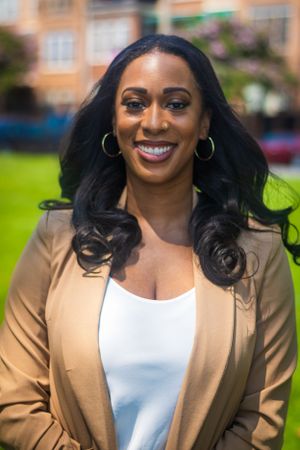 Professional portrait in a tan blazer and white top with statement hoop earrings outdoors.