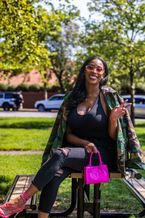 Casual outdoor fashion photo with camo jacket, black top, ripped jeans and bright pink accessories.