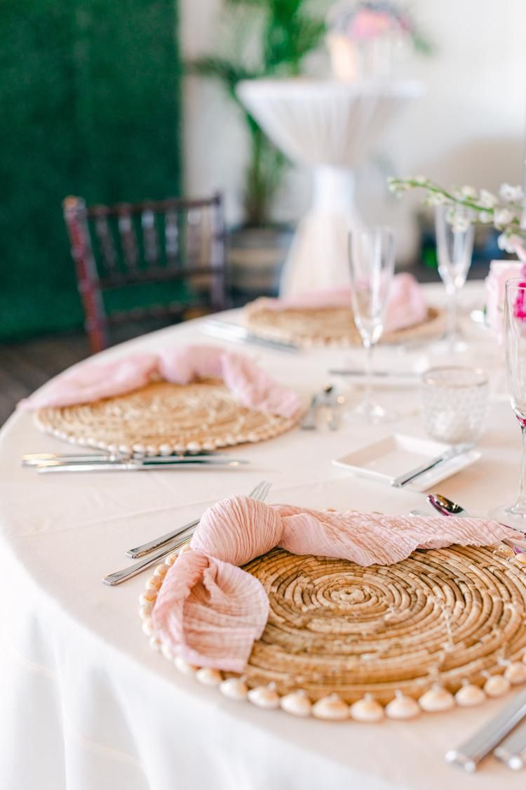 Elegant table setting with round woven placemats and pink napkins on white tablecloth at formal event.
