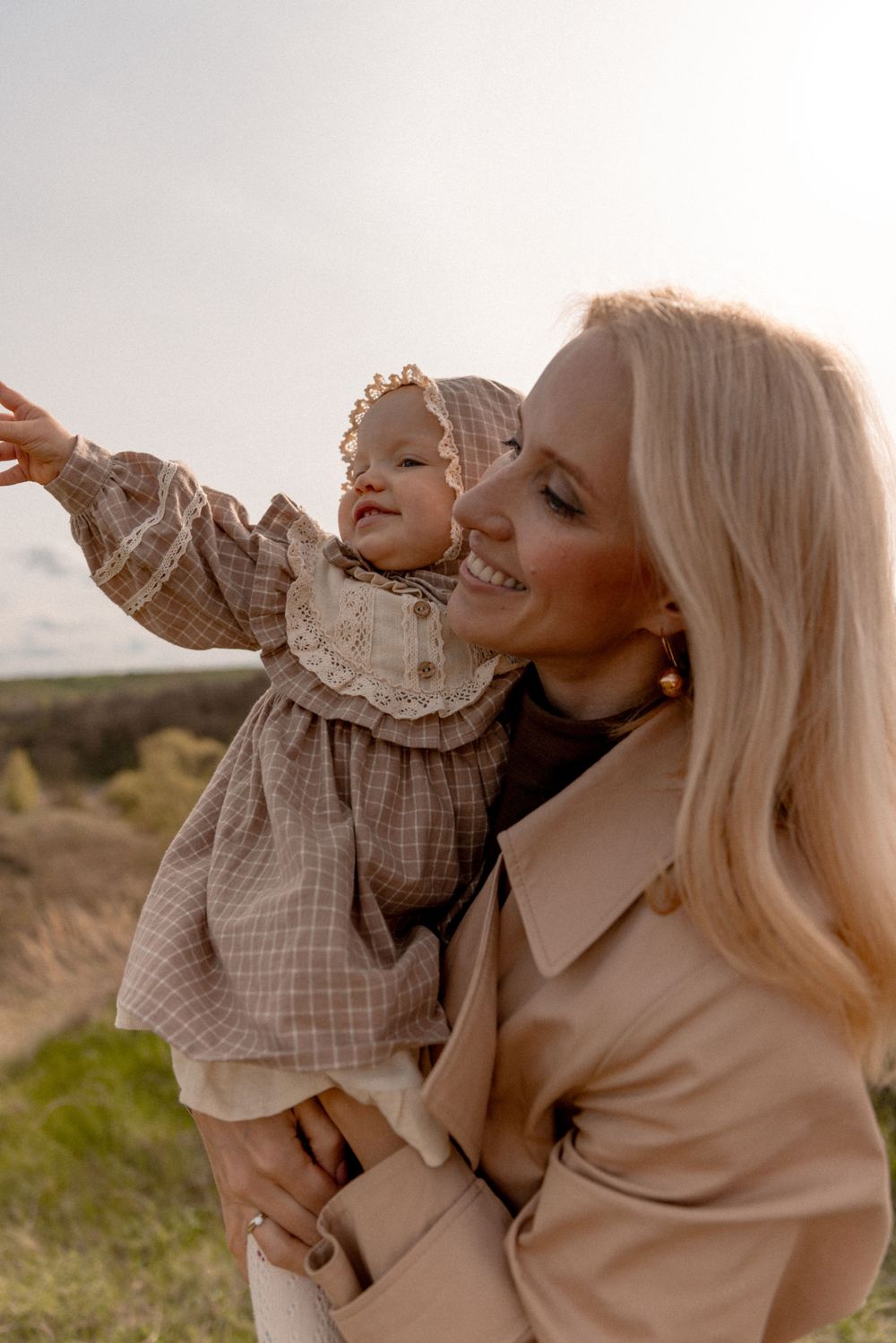 A parent and child share a tender outdoor moment at sunset while wearing warm neutral-toned clothing.