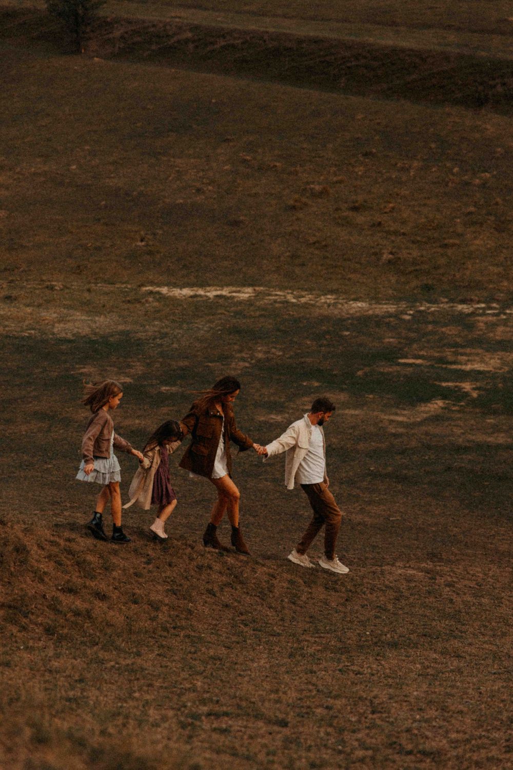 Four people walking together in a line along a brown hillside during golden hour, creating silhouettes against the landscape.