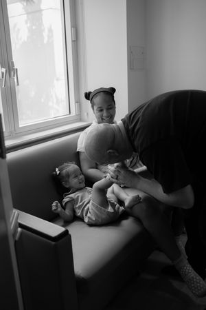 Black and white photo series showing tender moments between parent and infant on a couch near a window.