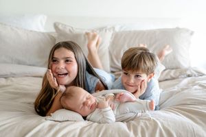 Happy children snuggle and play together on white bedding while laughing and having fun.