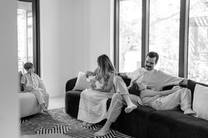 A monochrome series showing a family sitting and playing on a bed with natural light streaming through large windows.