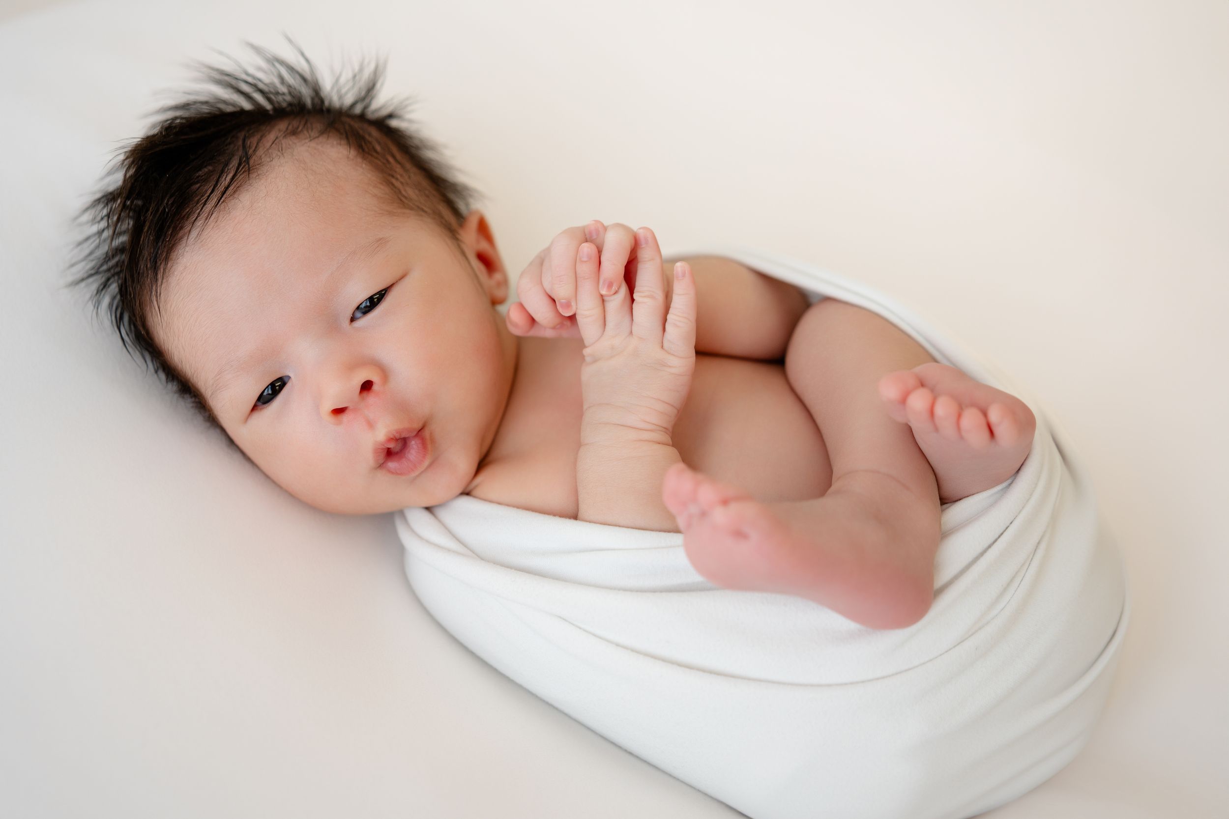 Adorable sleeping newborn baby swaddled in white blanket rests peacefully on soft bedding.