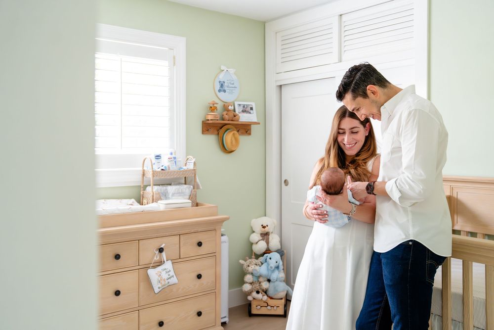 A couple stands together in a tender moment near wooden furniture in a nursery with mint green walls.