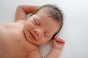 Peaceful sleeping newborn baby with closed eyes and tiny raised hand resting on white background.