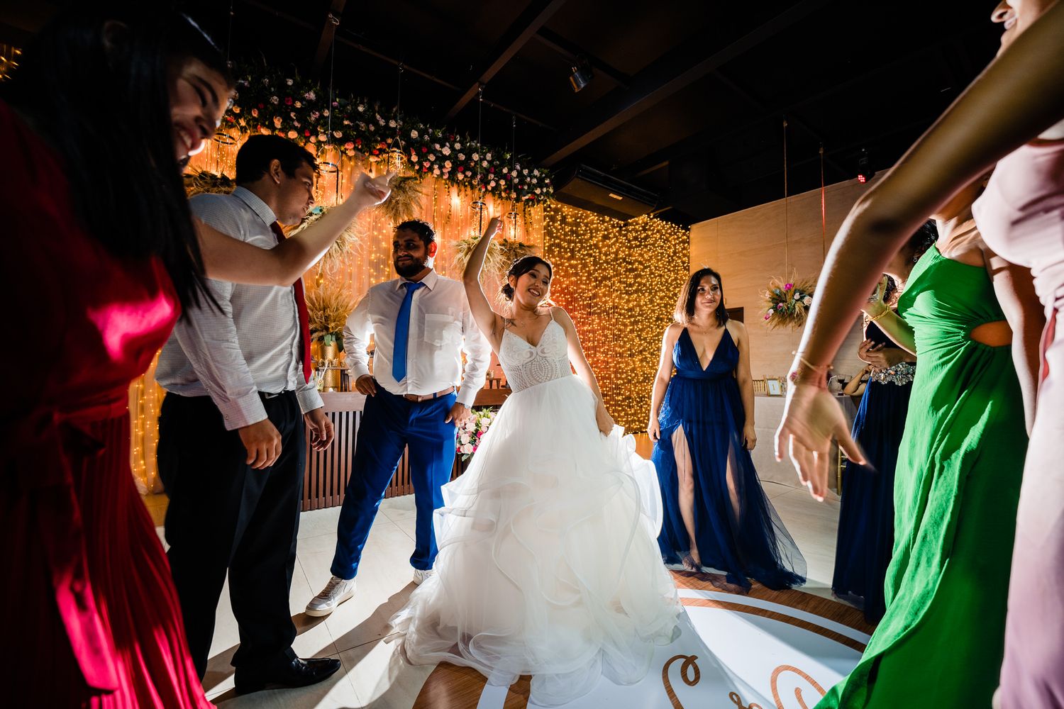 Joyful bride dancing with guests in a vibrant wedding celebration, surrounded by friends in colorful attire under warm festive lighting.