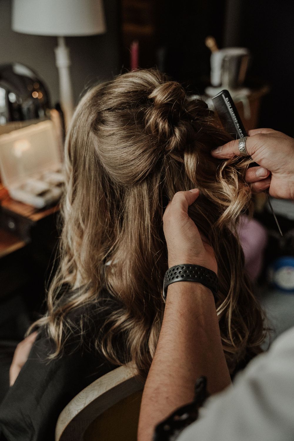 A hairstylist uses a curling iron to style long blonde hair in a dimly lit salon setting.