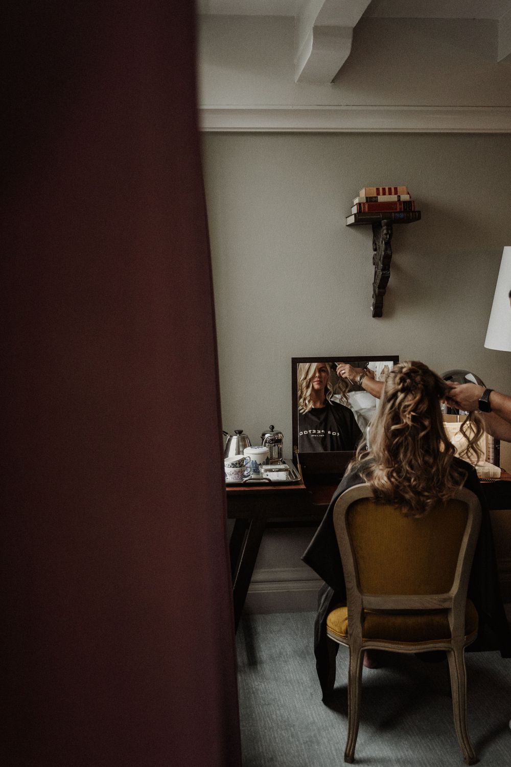 A person sits at a vintage desk with curled hair visible from behind in a moody, dimly lit room.