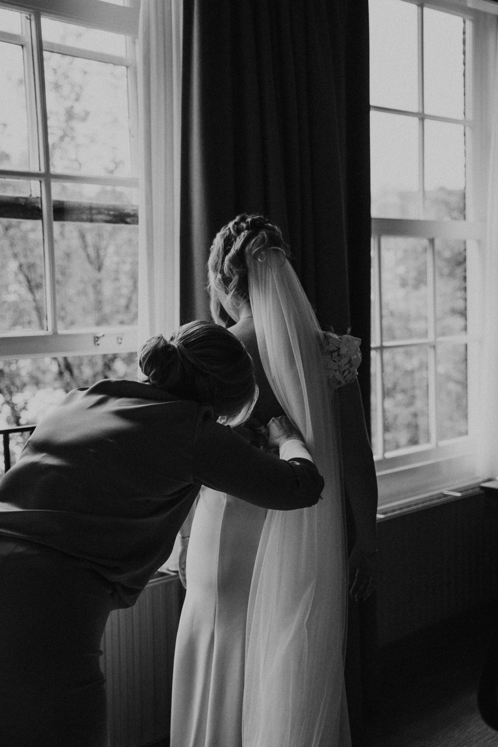 A tender wedding moment captured in black and white by a window with natural light streaming in.