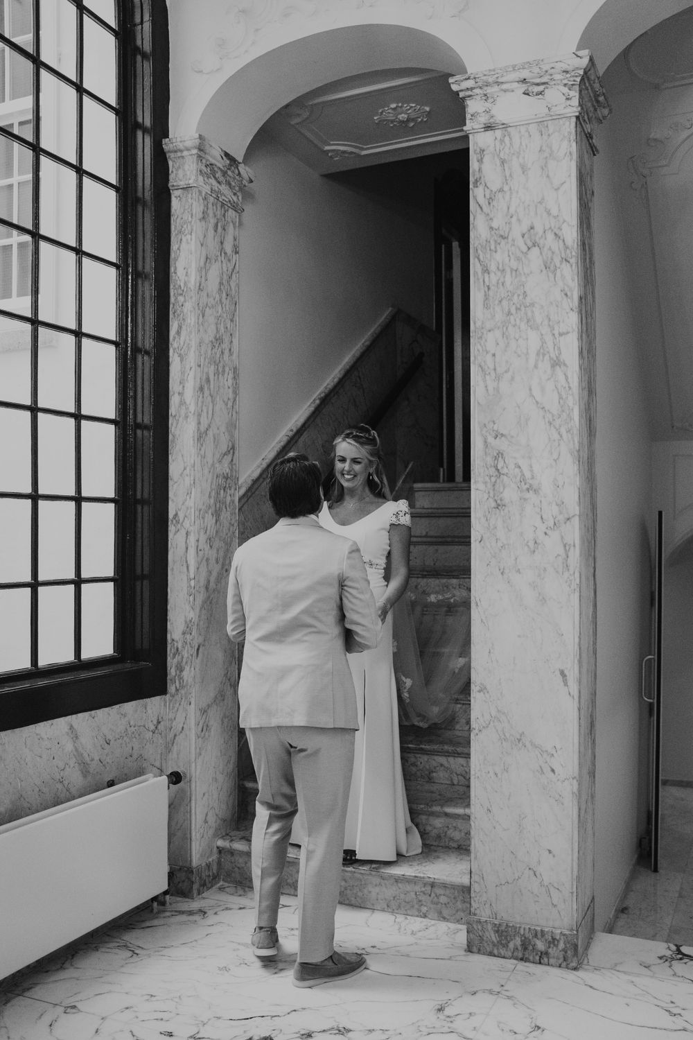 A couple shares a tender moment on marble stairs in an elegant archway with classical architecture.