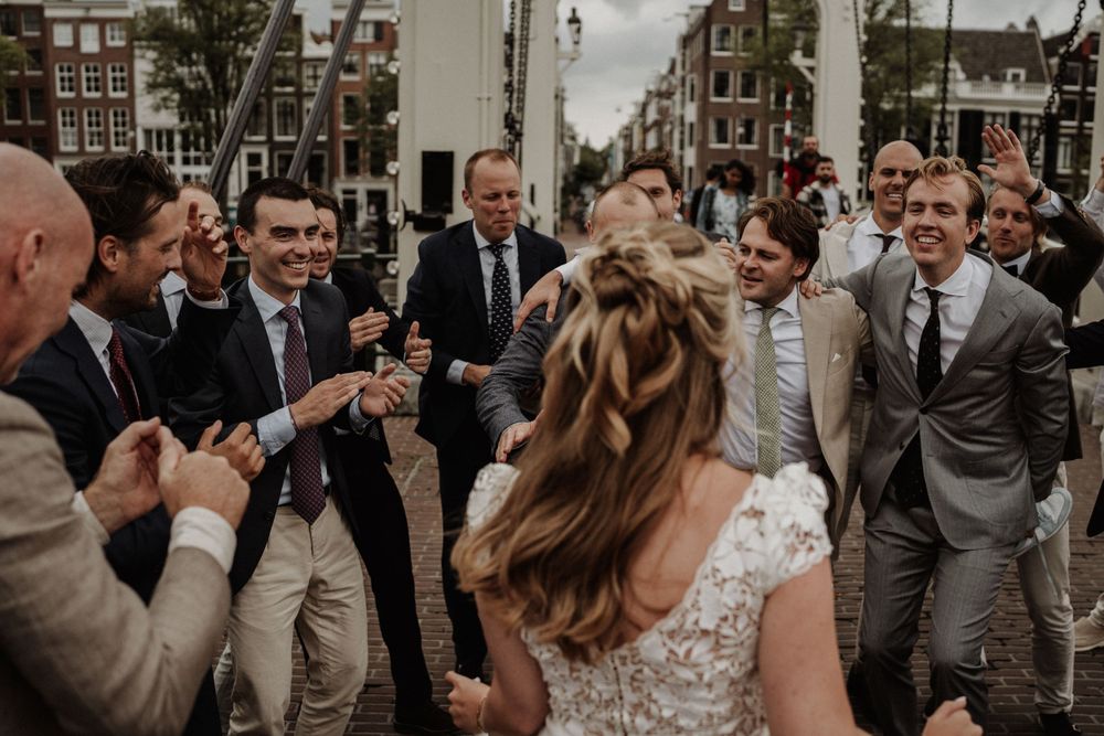 Wedding guests gather in a circle celebrating on a cobblestone street in Amsterdam with historic buildings in background.