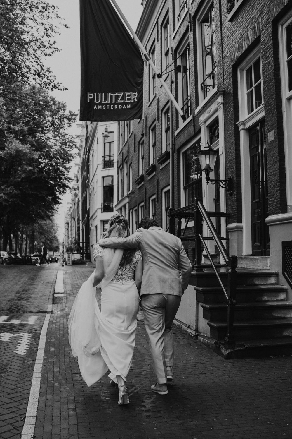 A couple walking down a cobblestone street in front of the Pulitzer building in black and white photography.