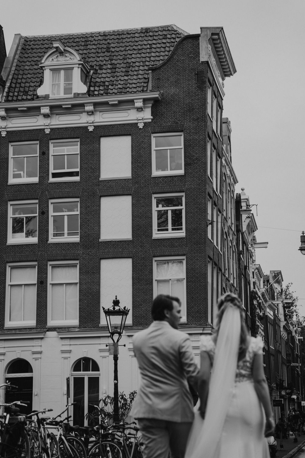 A black and white photo of a traditional brick building in Amsterdam with arched windows and a vintage street lamp.