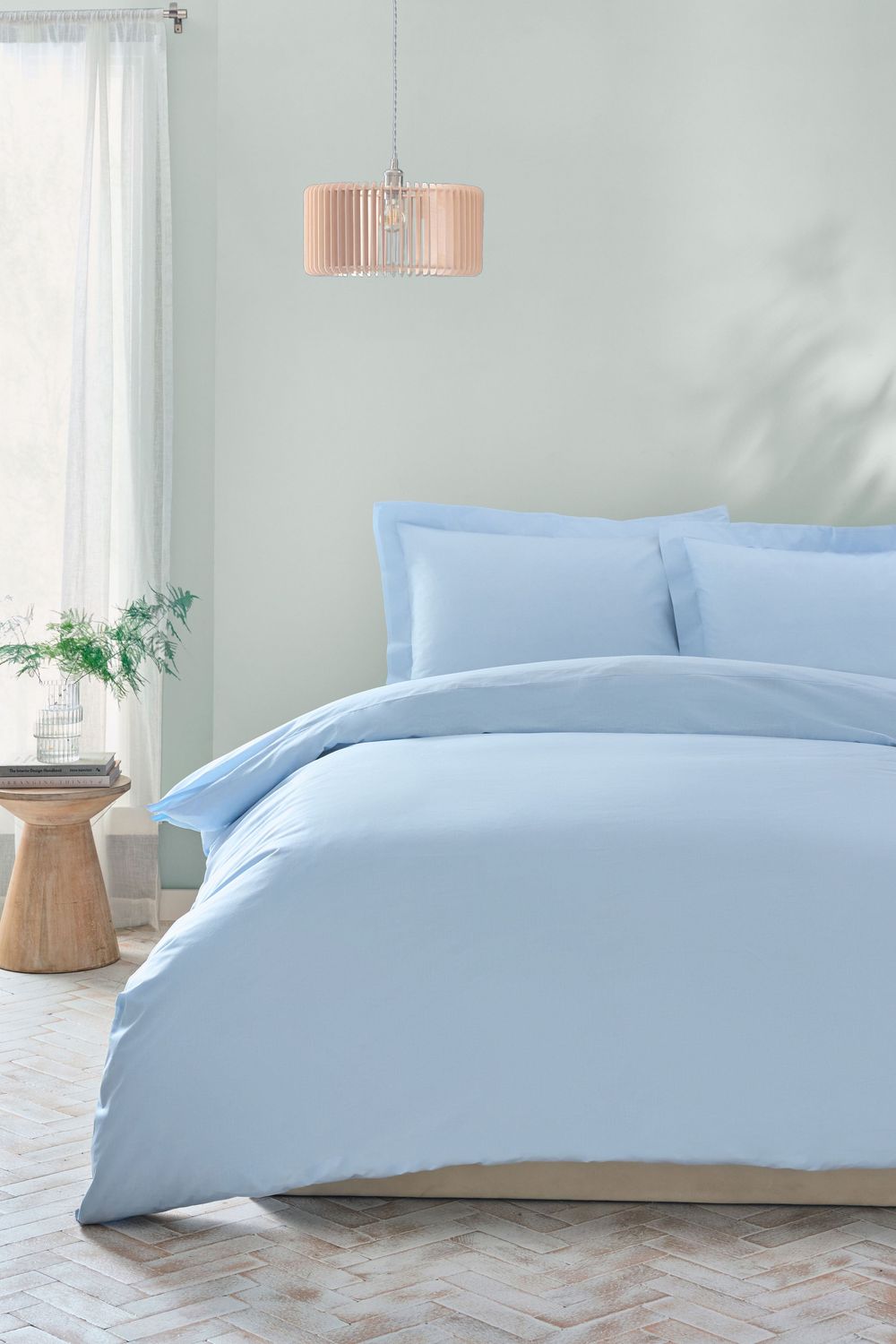 Light blue duvet cover set with matching pillowcases in modern bedroom with copper pendant light and wooden side table.
