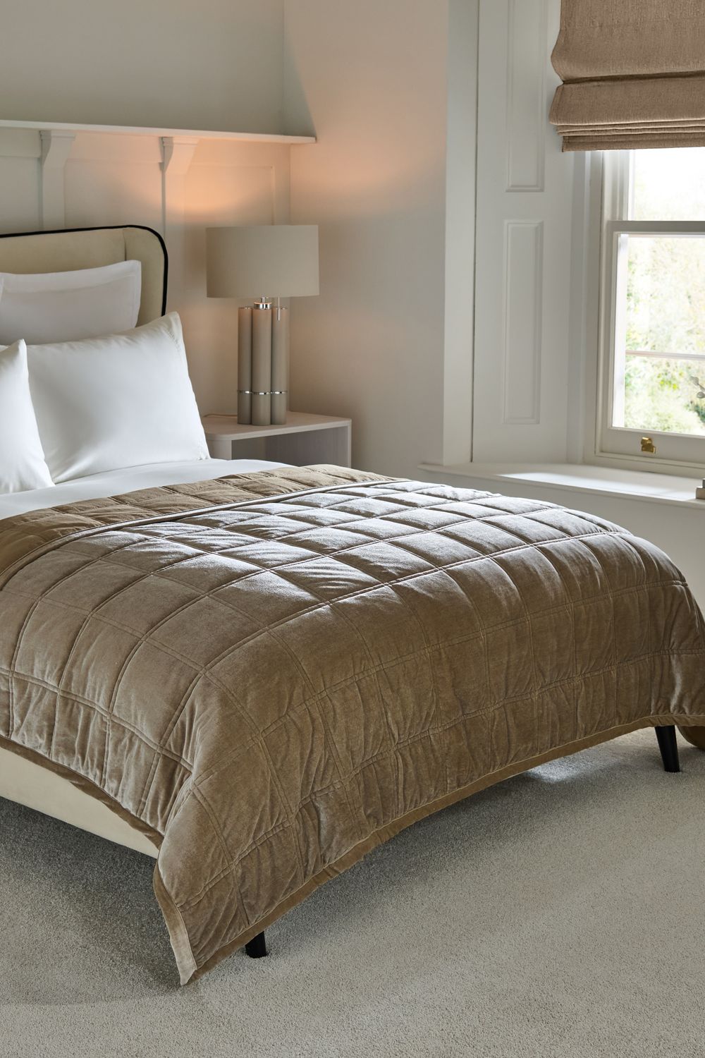 Plush brown velvet comforter on a clean white bed with modern table lamps and a window in a serene bedroom.