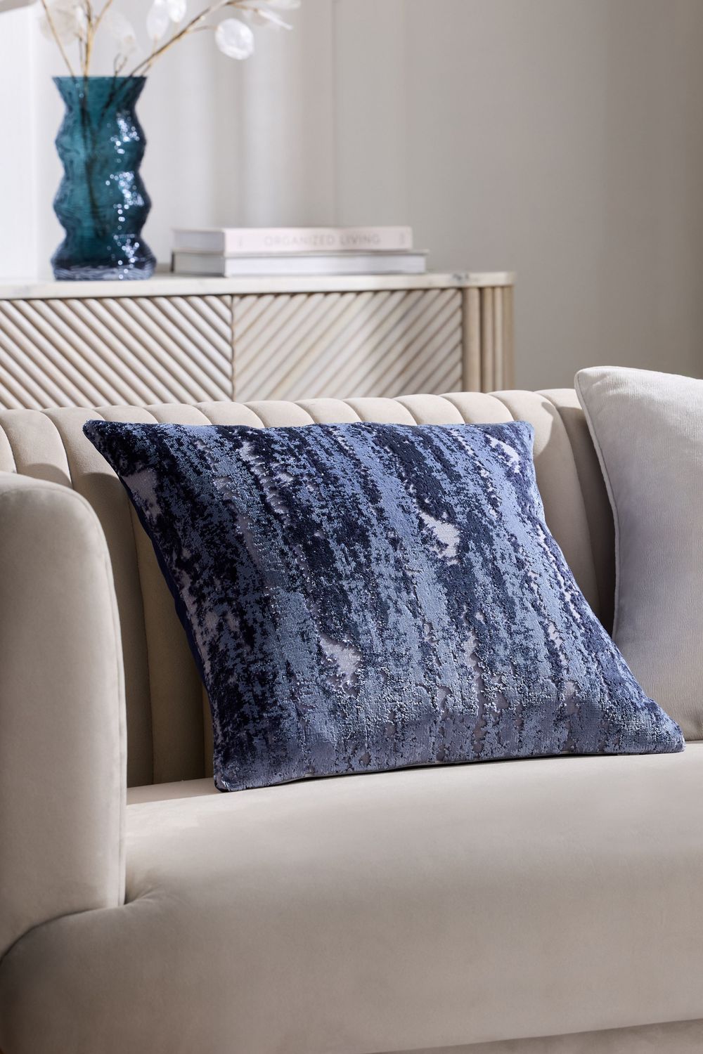 Plush navy blue velvet lumbar pillow arranged on a light beige contemporary sofa against neutral wall decor.