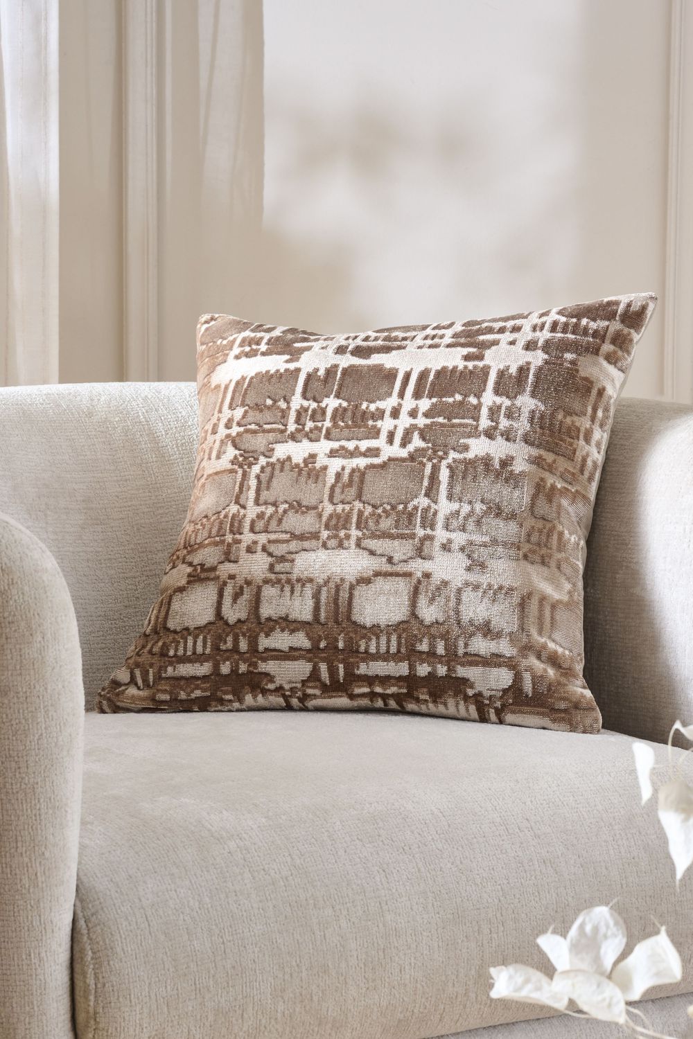 Close-up view of a modern grey couch with brown patterned throw pillows in a sunlit living room.