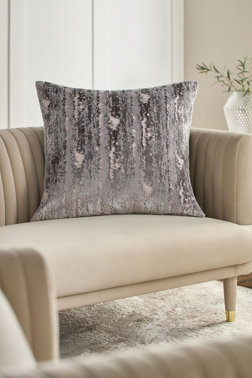 Luxurious gray velvet decorative pillow with distressed metallic pattern sits on beige channel-tufted accent chair.