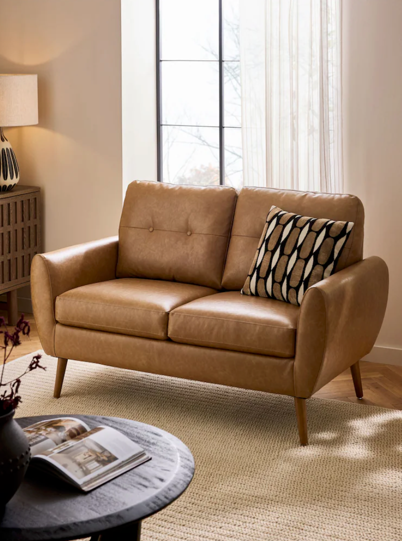 Modern tan leather sofa with black and white accent pillows sits elegantly against a bright window-lit wall.