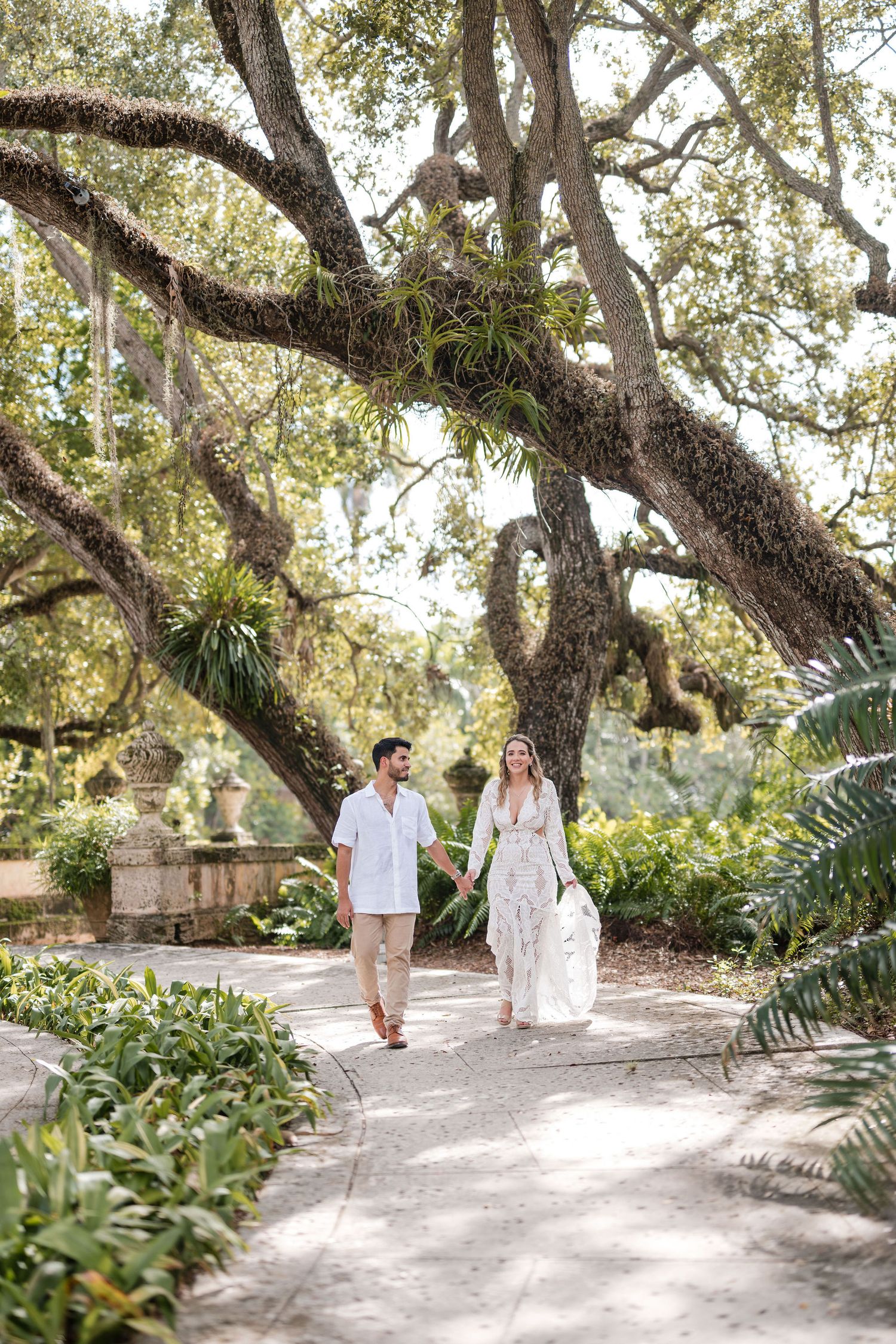 Couple walking under a tree canopy at the Vizcaya Museum and Gardens in Miami, FL during their engagement session by Gary Rosado Photography