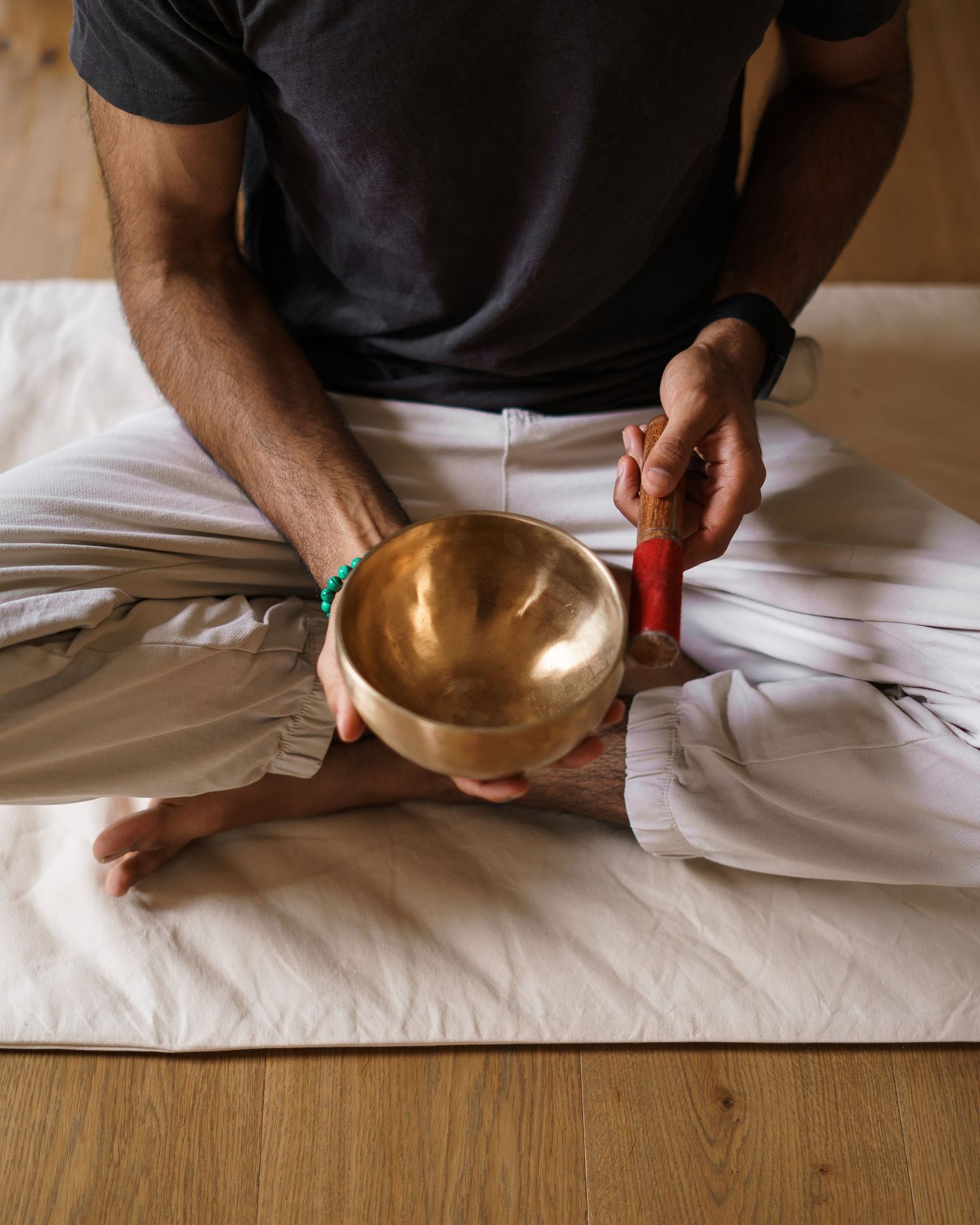 Man sitting cross-legged playing a Tibetan singing bowl with a red mallet during a meditation session.