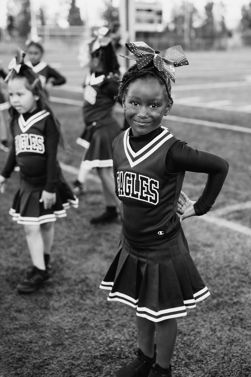 Young girl in Eagles cheerleader uniform posing confidently on football field in black and white.