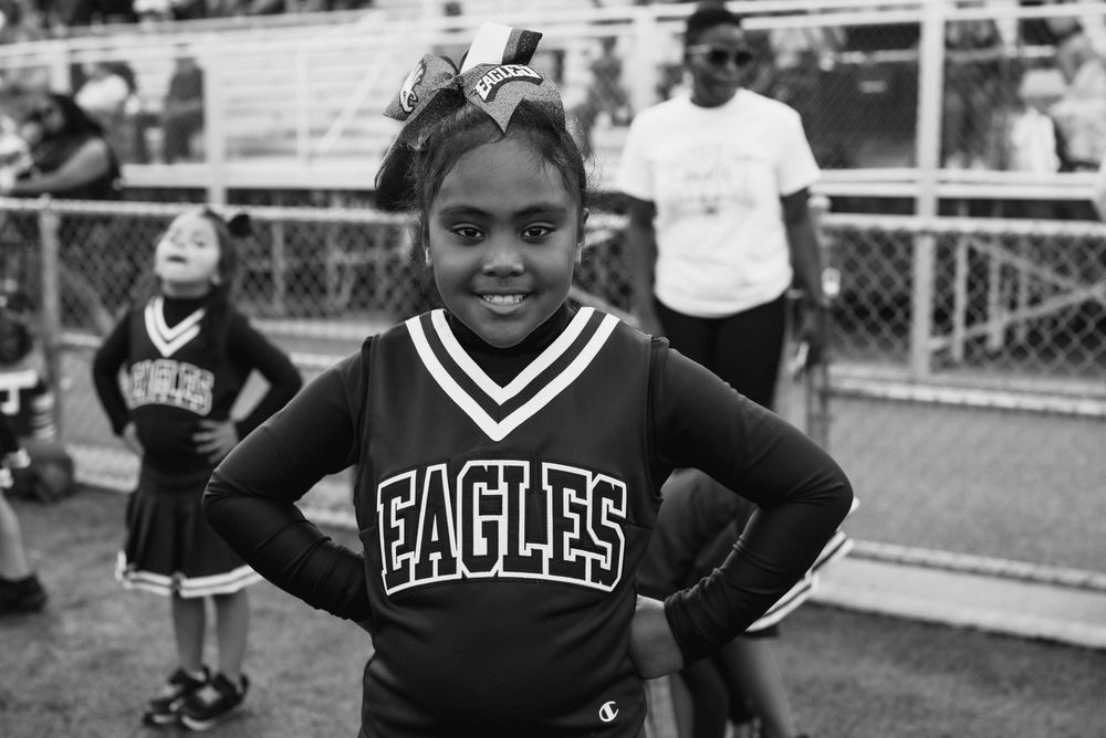 Smiling girl in Eagles cheerleader uniform posing confidently at outdoor sports event.